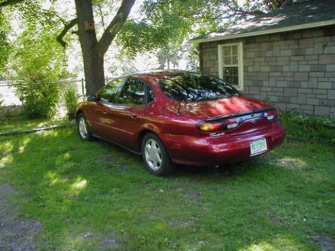 1997 Ford Taurus - A red sedan is parked on a grassy lawn next to a house.