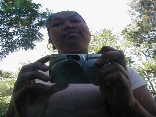 Person taking a selfie in a car's side mirror, holding a digital camera