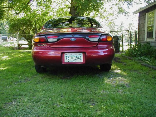 red Ford Taurus parked in a grassy yard, rear view. License plate reads 46 D 1541