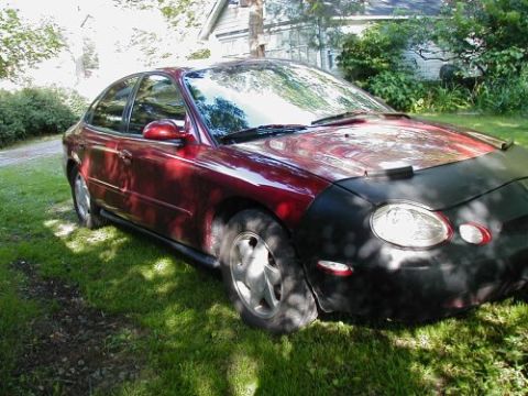 1997 Ford Taurus - A 1997 Ford Taurus sedan is parked on a grassy lawn, partially covered by a car bra.