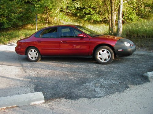 red sedan parked outside, front end covered by a black car bra