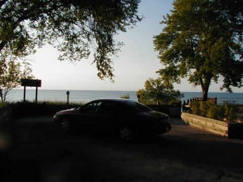1997 Ford Taurus - A dark sedan is parked near a body of water, with trees and a sign in the background.