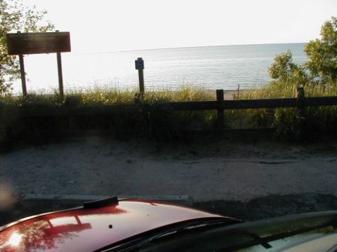 1997 Ford Taurus - A view of the beach and water from a parking area, with the hood of a red car visible.