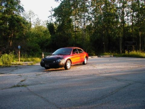 1997 Ford Taurus - A red 1997 Ford Taurus sedan is parked in an outdoor lot with trees visible.