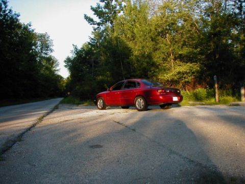1997 Ford Taurus - Red 1997 Ford Taurus parked on the side of a road with trees in the background.