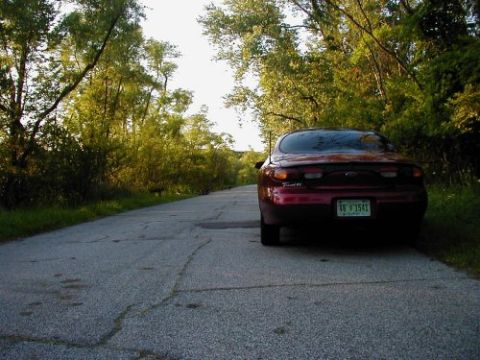 1997 Ford Taurus - Rear view of a red 1997 Ford Taurus on a tree-lined rural road.