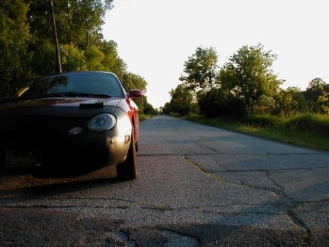 1997 Ford Taurus - A red 1997 Ford Taurus is parked on the side of a rural road, viewed from a low angle.