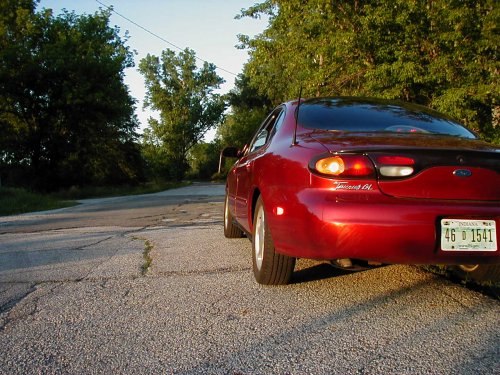 1997 Ford Taurus rear view on a cracked asphalt road with trees in background
