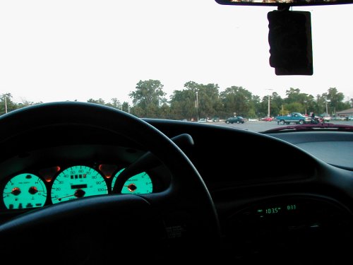 1997 Ford Taurus interior view showing dashboard, glowing green gauges, and digital clock. Other vehicles visible in parking lot