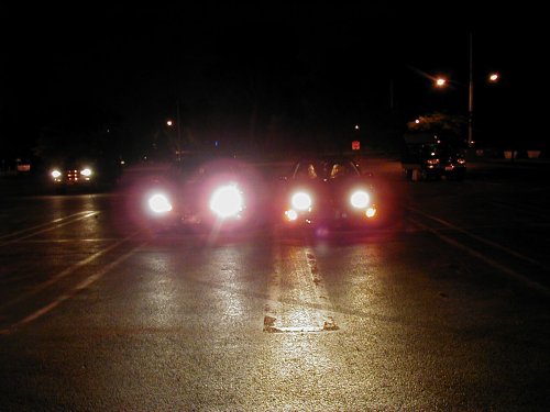 Multiple cars driving on a wet road at night, headlights illuminating the scene