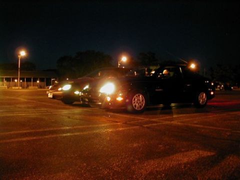 1997 Ford Taurus - Several cars are parked in a lot at night, with streetlights illuminating the scene.