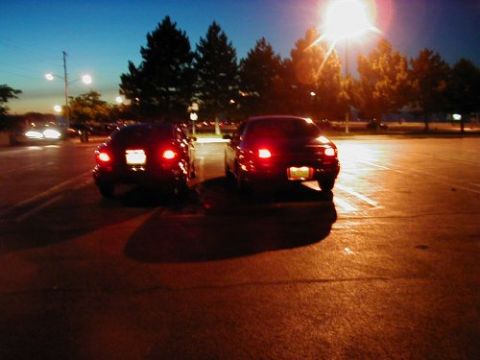 1997 Ford Taurus - Two cars sit in a parking lot as the sun sets, their brake lights illuminated.
