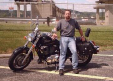 1989 Ford Bronco - Man poses with his motorcycle in an outdoor lot with a bridge in the background.