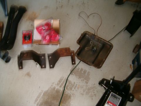 1979 Ford Bronco - Various vehicle parts including exhaust pipes and a transmission pan are laid out on a garage floor.