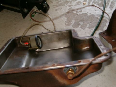 1979 Ford Bronco - A close-up view of an oil pan with a connected gauge and wiring, resting on a concrete surface.
