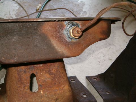 1979 Ford Bronco - A close-up view of a rusty oil pan with a sensor and wiring, attached to metal brackets.