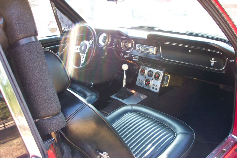 Vintage Mustang interior with wood-rim wheel, floor shifter, console gauges and black bucket seats