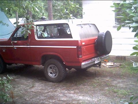 1985 Ford Bronco - This 1985 Ford Bronco is seen from the rear quarter angle, a red body with a white top and a spare tire mounted on the tailgate.