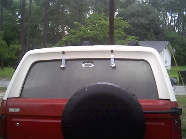 Rear of red and white SUV with white hardtop and black spare tire cover, parked in wooded yard