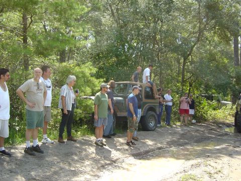1993 Ford Bronco - Group observes off-road vehicles in a wooded area with muddy terrain.