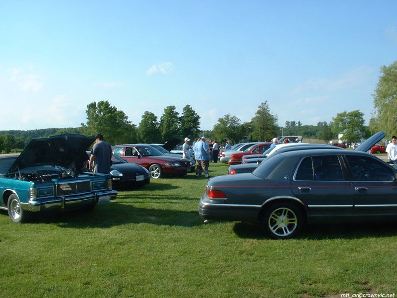 Grey Mercury Grand Marquis on gold wheels among cars at a grass-field car show