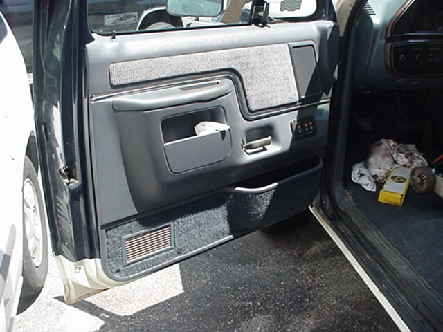 1989 Ford Bronco interior door panel with storage pocket and floor mat. A yellow box and some rags are on the floor