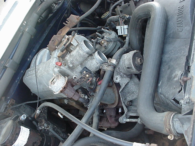 Engine bay with visible hoses, wiring, and engine components. A radiator hose has a "CAUTION" label