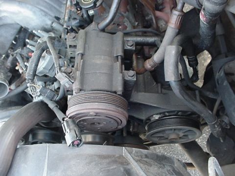 1989 Ford Bronco - Close-up view of the engine bay, focusing on the air conditioning compressor and associated pulleys.