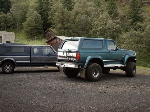 1996 Ford Bronco - Two Ford trucks, a Bronco and a pickup, are parked outdoors near some buildings and trees.