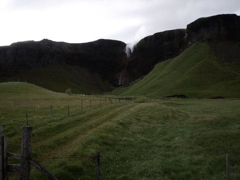 1996 Ford Bronco - A waterfall flows down a cliff in a green valley, with a path and fence in the foreground.