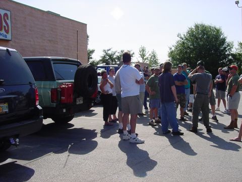 1986 Ford Bronco - A group of people stand around a green Ford Bronco and a dark SUV in a parking lot.