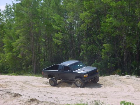 1986 Ford Bronco - This dark gray pickup truck navigates a sandy terrain with its off-road tires visible.