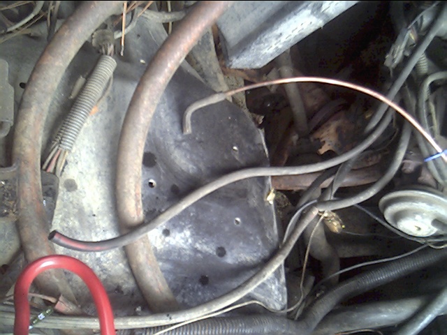 Engine compartment with hoses, wires, and metal components. A red loop is visible in the lower left