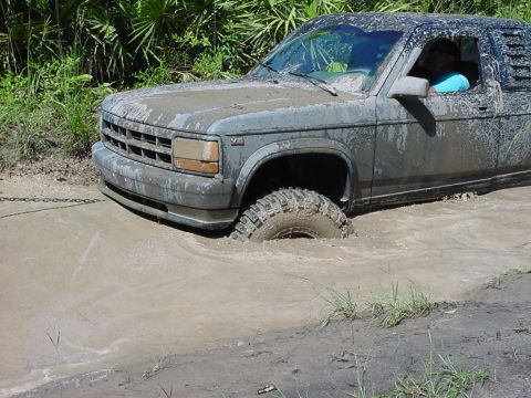 1986 Ford Bronco - This truck is deep in the mud, with only its roof and part of the cab visible above the mire.