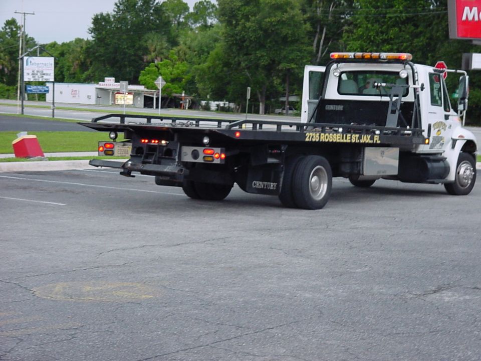 White Century tow truck with a black flatbed, parked on asphalt. Text on the side reads '2735 ROSSELLE ST. JAX. FL'
