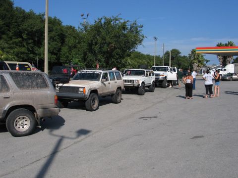 1995 Ford Bronco - A group of off-road vehicles are parked in a line at a gas station under a bright blue sky.