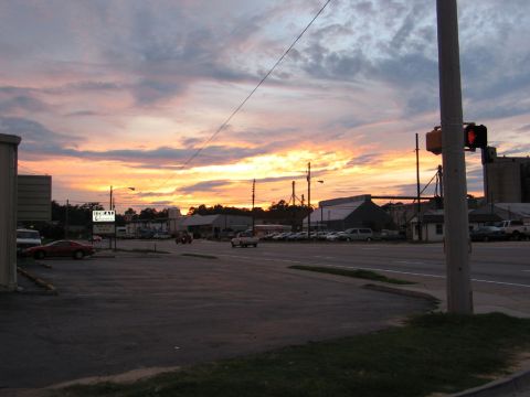 1995 Ford Bronco - A parking lot scene unfolds under a dramatic sunset, with various vehicles and commercial buildings visible.