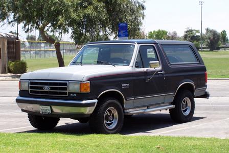 1990 Ford Bronco - This Ford Bronco is parked in a grassy area with trees and a fence in the background.