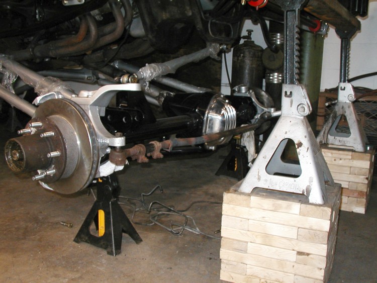 Front solid axle with disc brake rotor and radius arms on jack stands in a garage
