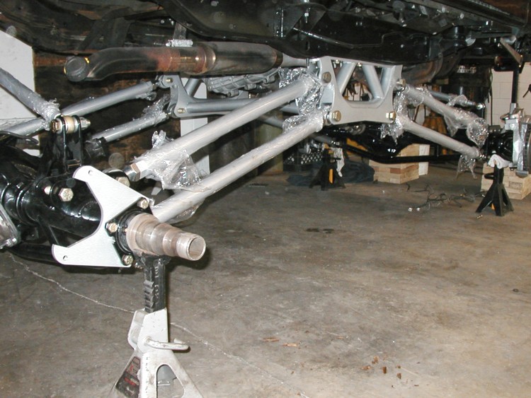 Underside of raised chassis showing gray custom suspension links, brackets and axle stub on jack stands