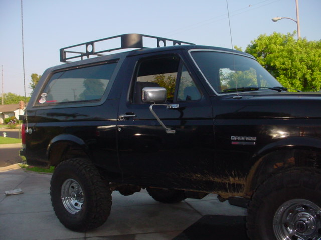 Lifted black Ford Bronco side view with roof rack, chrome mirrors and mud-streaked doors