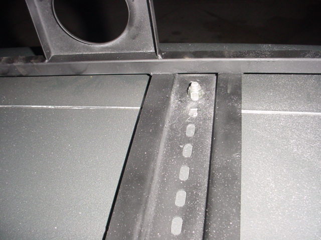Close-up of a metal bracket with a bolt and slotted holes, part of a roof rack system