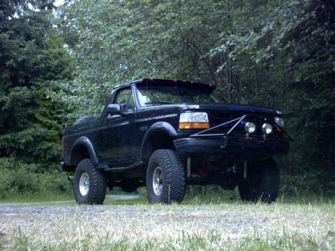 1995 Ford Bronco - A black Ford Bronco with a custom front bumper and off-road tires sits on a gravel path.