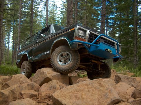 1978 Ford Bronco - A dark green 1978 Ford Bronco navigates a rocky trail with a prominent blue winch bumper.