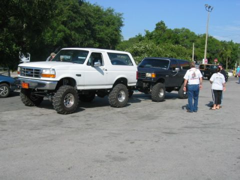 1992 Ford Bronco - A lifted white 1992 Ford Bronco is seen alongside another SUV at an outdoor event.