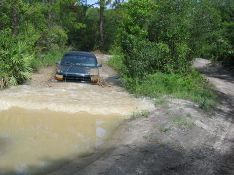 1992 Ford Bronco - This 1992 Ford Bronco navigates a challenging muddy water crossing on a dirt road.