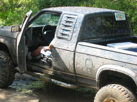 1992 Ford Bronco - A muddy pickup truck sits off-road with its driver's door open and a person visible inside.