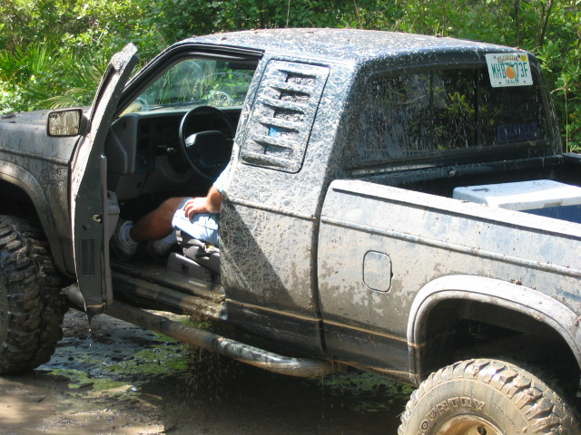 Mud-covered lifted pickup with driver door open and person lying across the seat