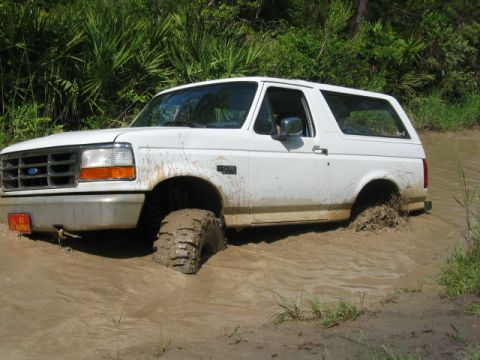 1992 Ford Bronco - White 1992 Ford Bronco navigating through a muddy off-road trail.