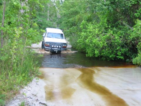 1992 Ford Bronco - A white 1992 Ford Bronco navigates a water crossing on a wooded trail.